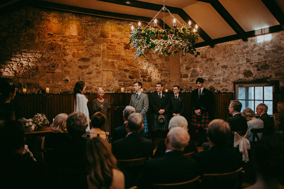Wedding ceremony taking place inside Rosebery Steading with guests seated in the candlelit barn