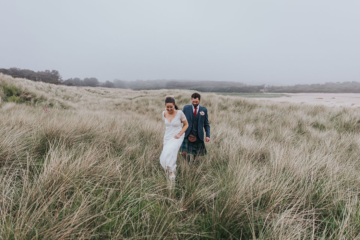 bride leads groom through grassland with sand in the background at harvest moon holidays