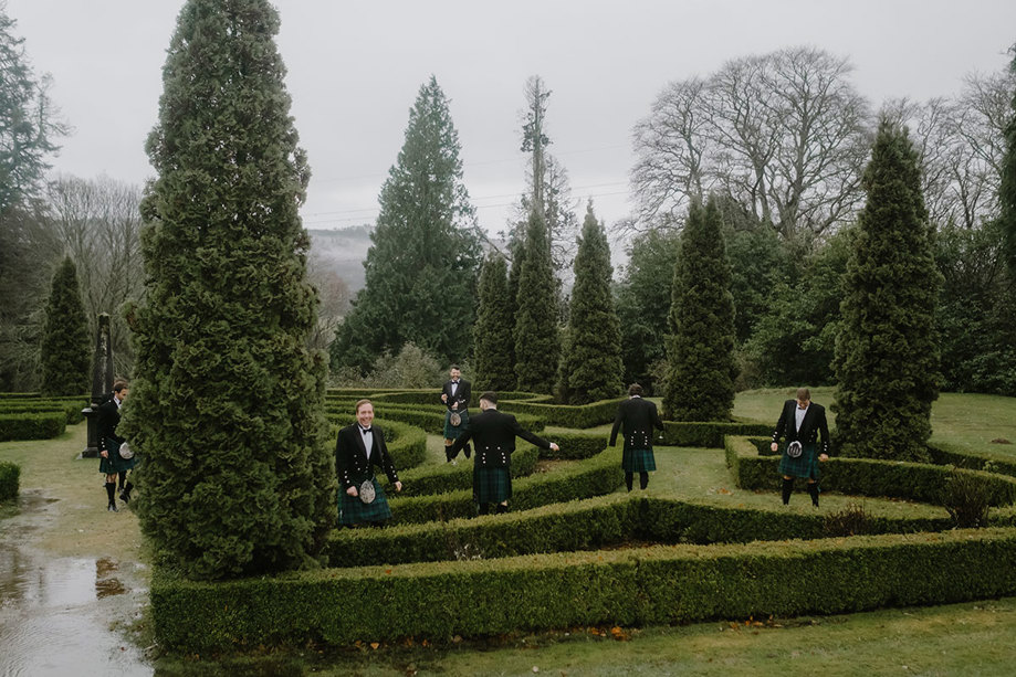 men in kilts standing in an outdoor maze.