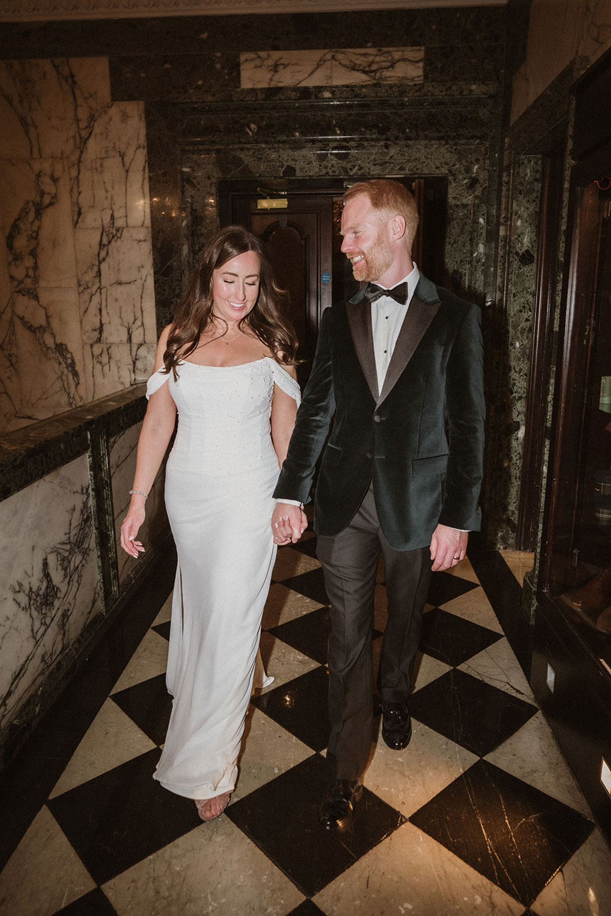 a smiling bride and groom walking hand-in-hand across a black and white checked floor at the Scotsman Hotel