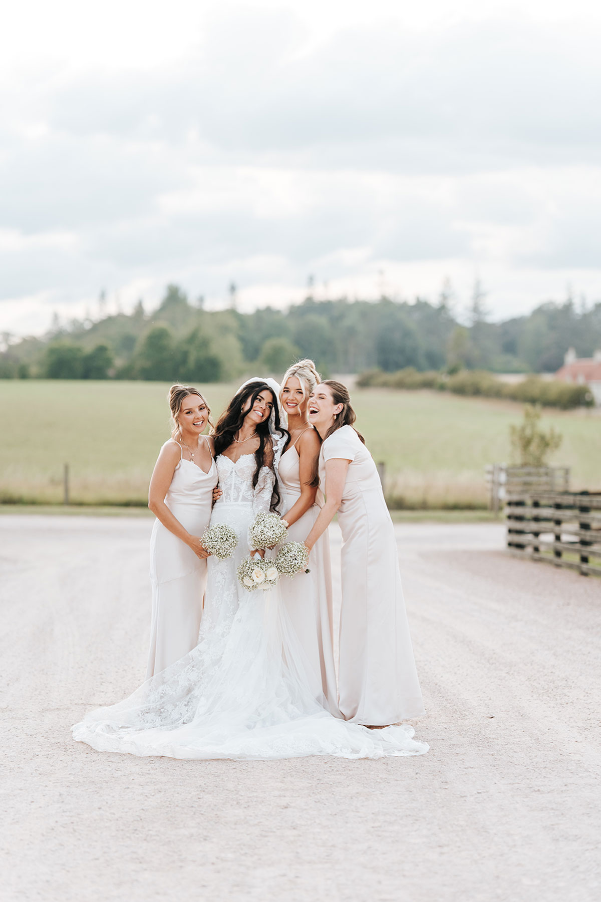 Bride and bridesmaids posing together outdoors in soft neutral dresses at a countryside wedding