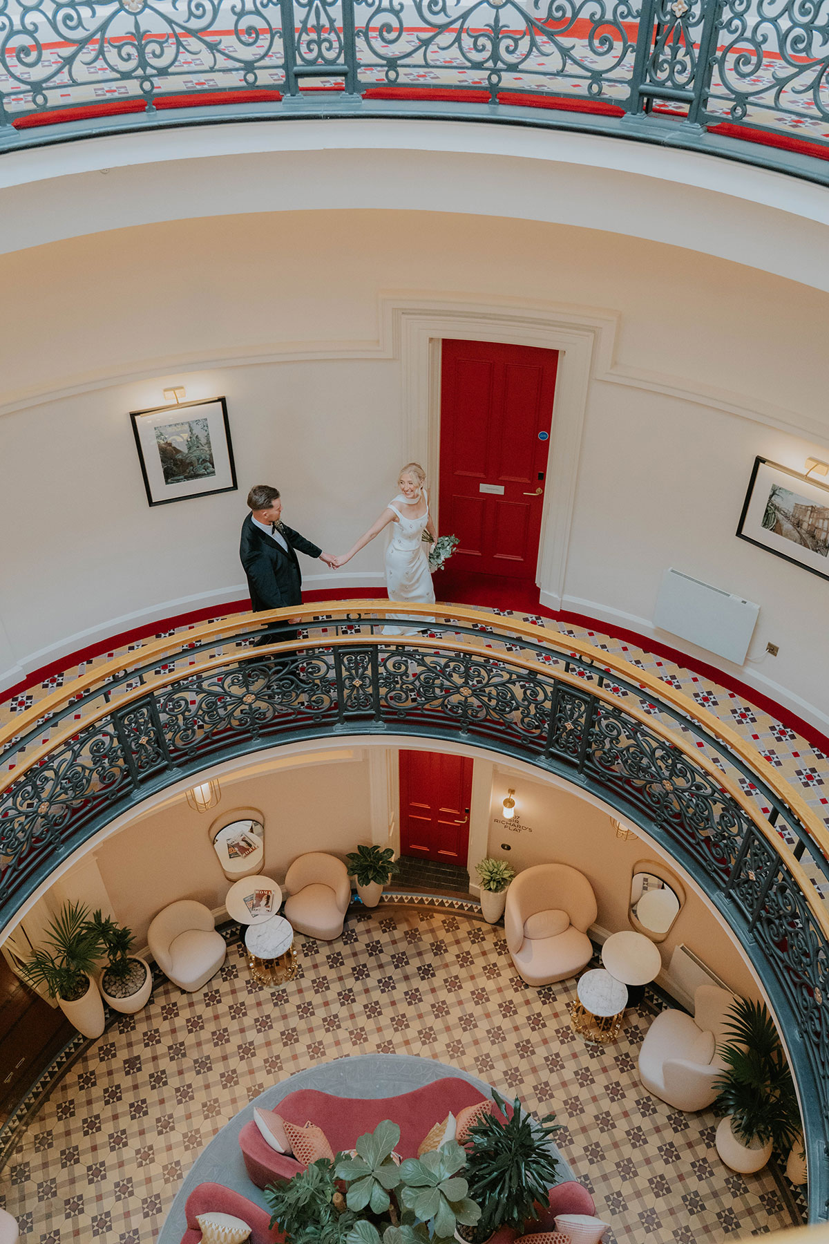 Bride and groom walking hand in hand around an ornate circular balcony inside their Edinburgh wedding hotel