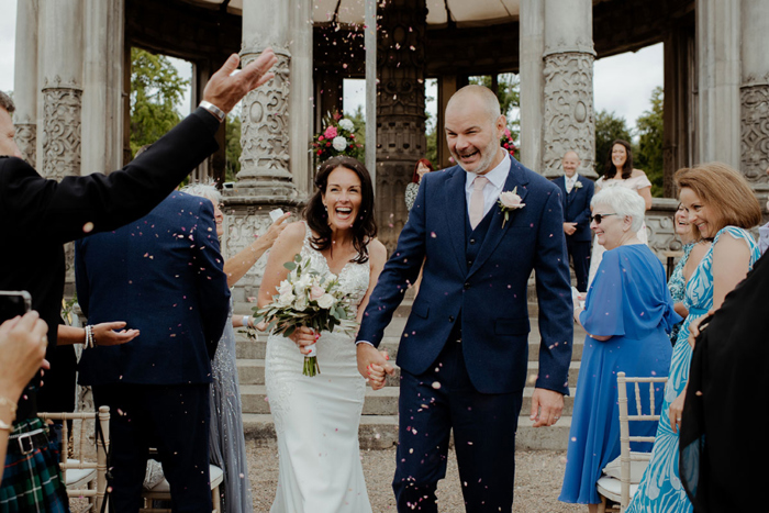 Smiling couple walk through confetti shower after ceremony