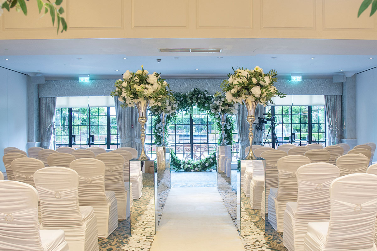 Indoor wedding ceremony setup at Western House Hotel, with white chair covers and floral arch at the aisle end.