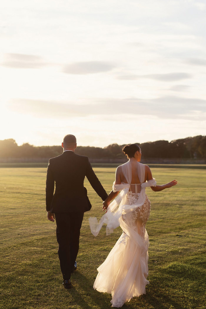 A bride and groom walking on grass.