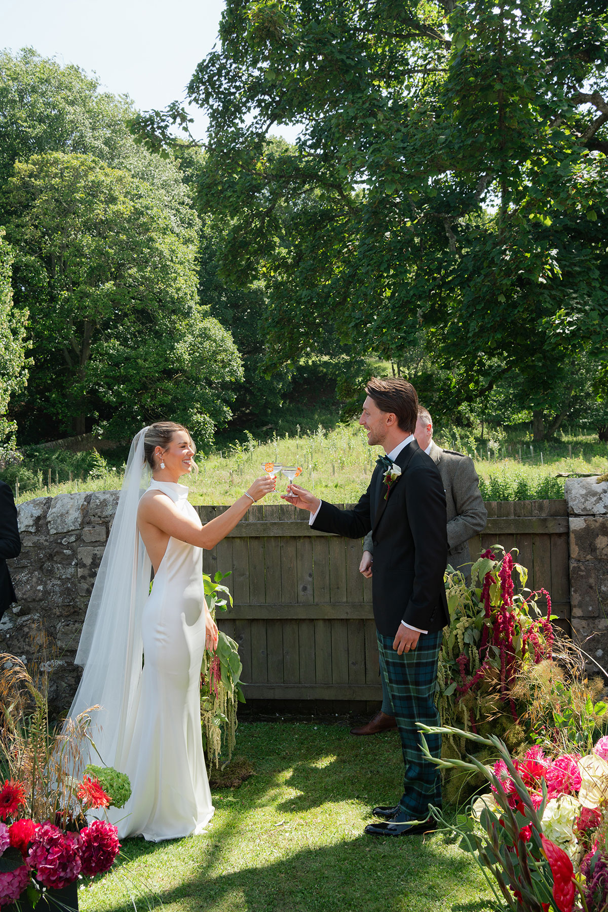 Bride and groom toast with paloma cocktails during their outdoor ceremony at Kinkell Byre, surrounded by colourful floral arrangements.