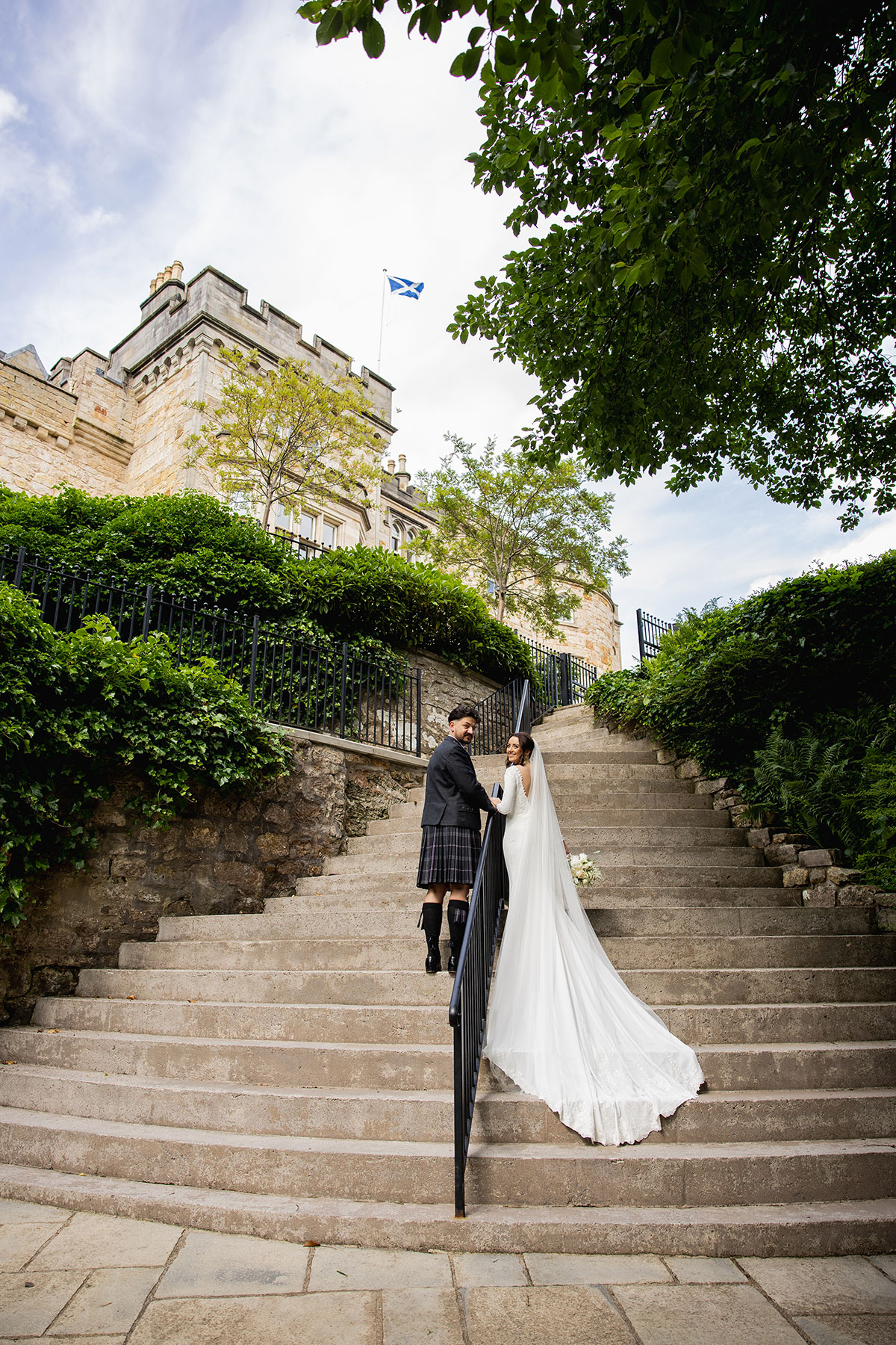 Couple pose on the sweeping outdoor staircase leading up to the castle, the bride’s train trailing behind her