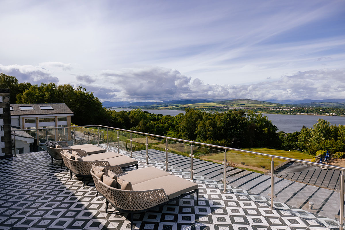 Terrace with patterned black-and-white tiled flooring and cushioned loungers facing a scenic view over a river and green hills
