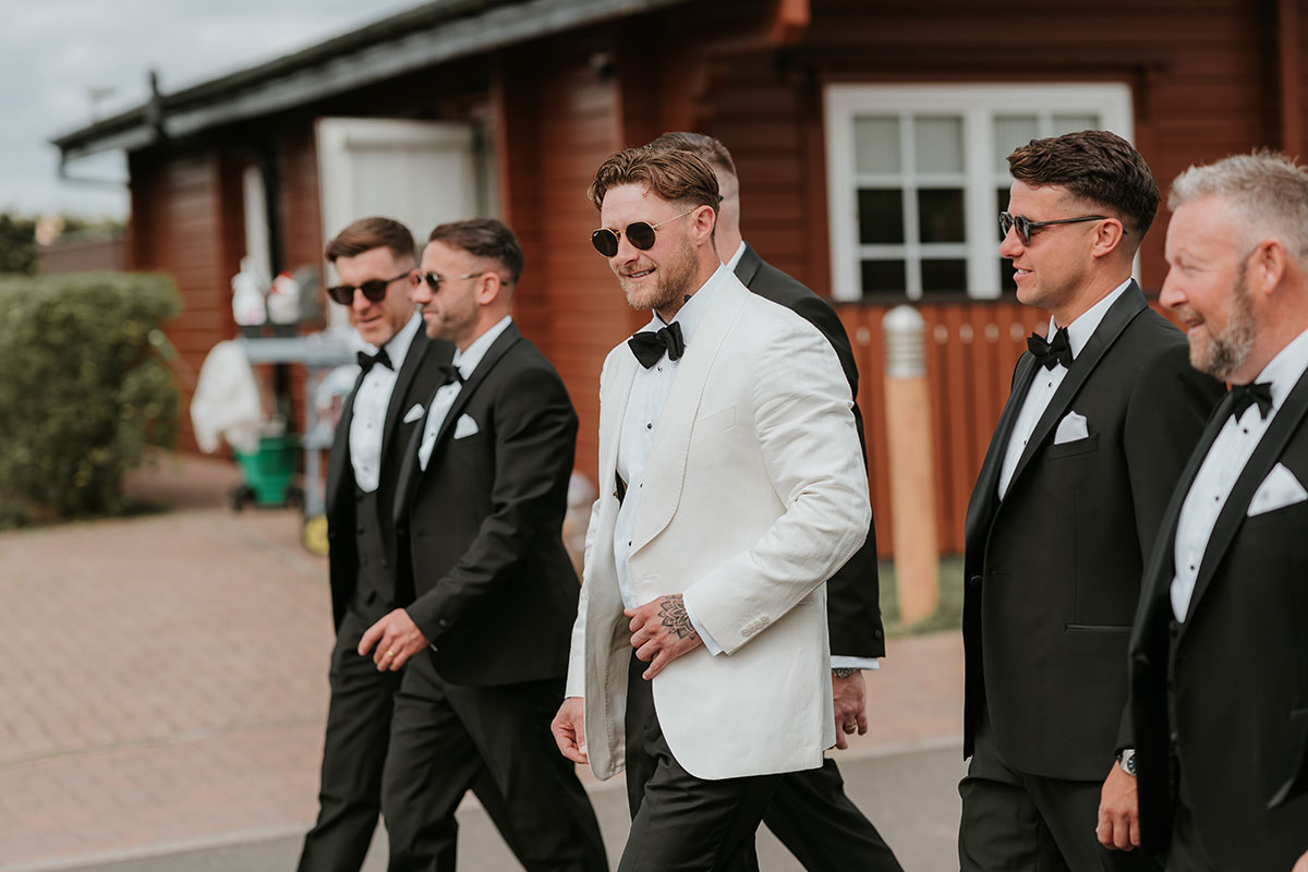 Groom and groomsmen walking together in tuxedos outside Ingliston Country Club wedding venue
