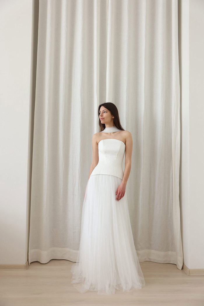 brunette model wears white dress with strapless corset bodice and floor length tulle skirt with a matching tulle scarf around her neck