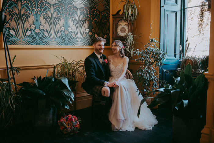 a bride and groom seated and posing for a photo in a teal and yellow decorated room at Netherbyres House with potted plants either side of them