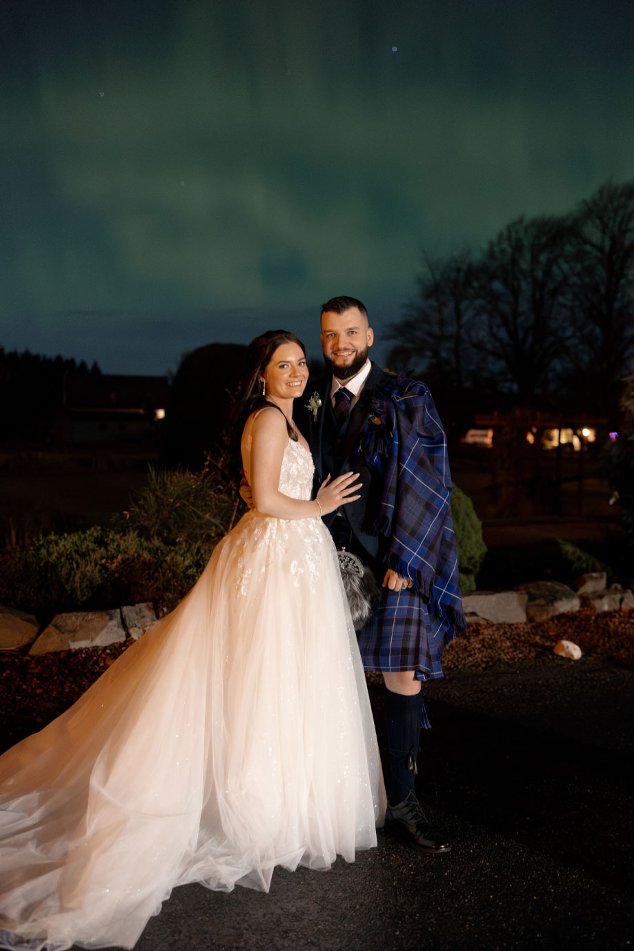 a bride and groom posing as the northern lights light up the sky