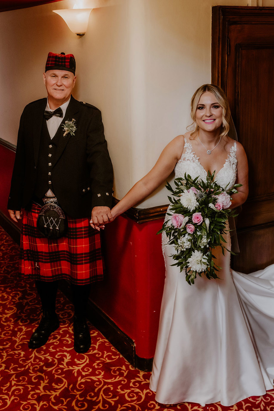  bride and dad hold hands and smile for picture at dalhousie castle