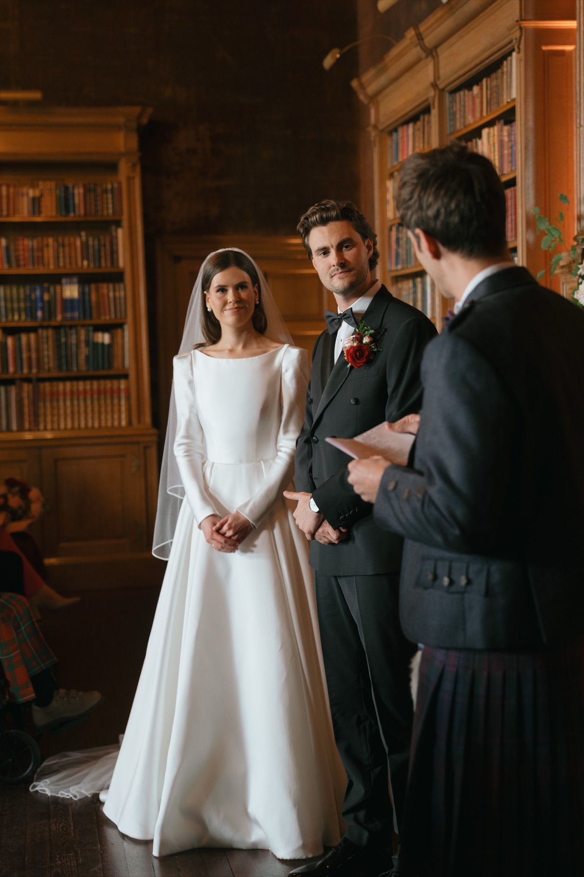 Nicole and Ryan stand together during their Barnbougle Castle wedding ceremony, with their celebrant and pink-and-red floral arrangements behind them.