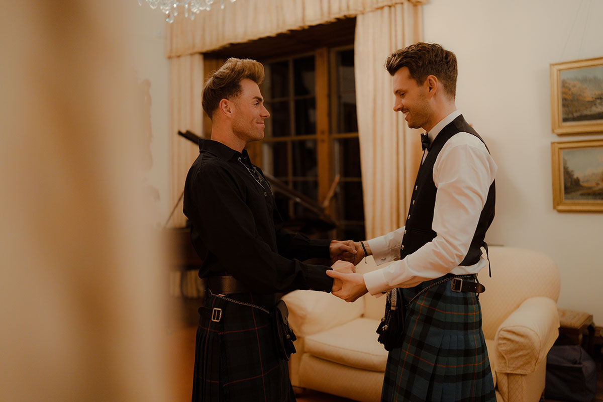 Two grooms share a private first look indoors at Newhall Estate, both wearing Gunn tartan kilts by MacGregor and MacDuff ahead of their evening celebrations