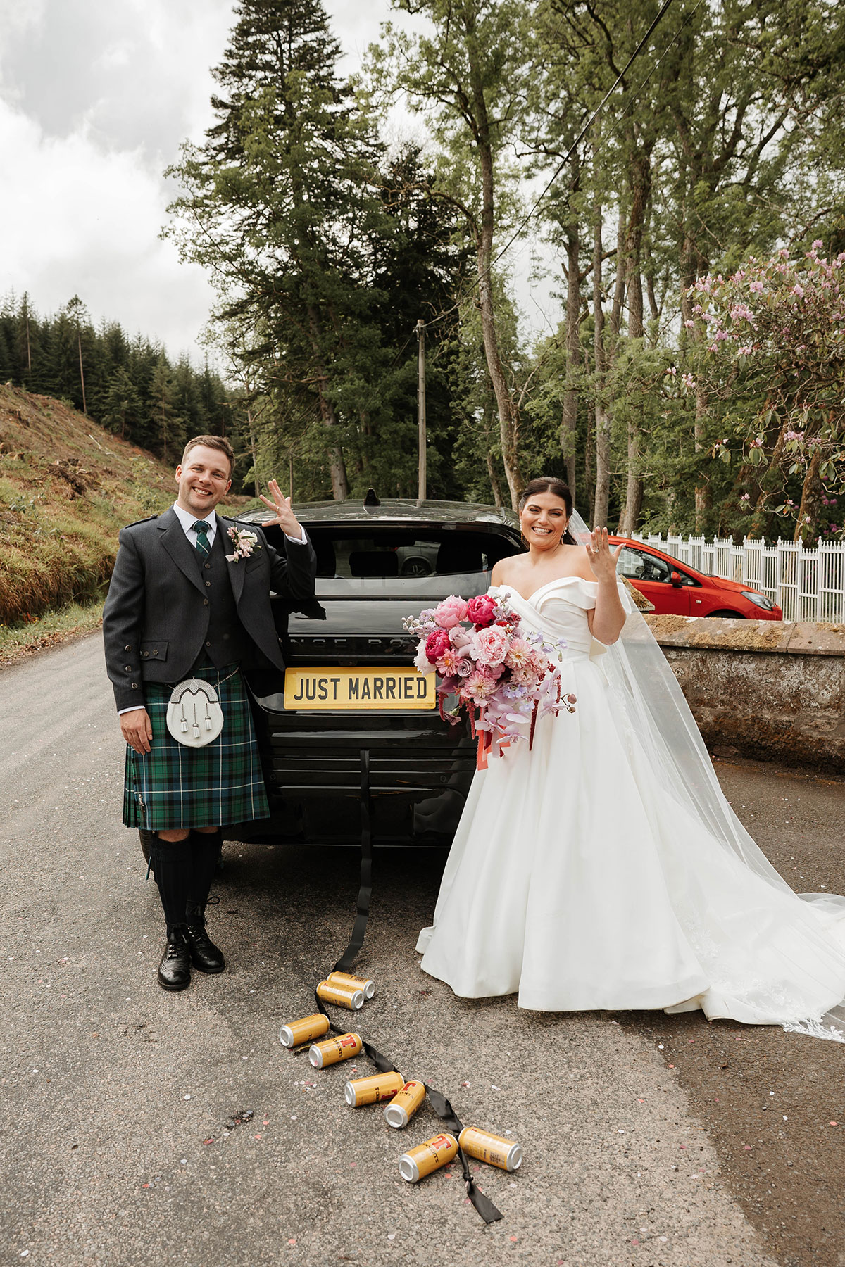 Newlyweds beside just married wedding car with beer can trail outside Drumtochty Castle Aberdeenshire