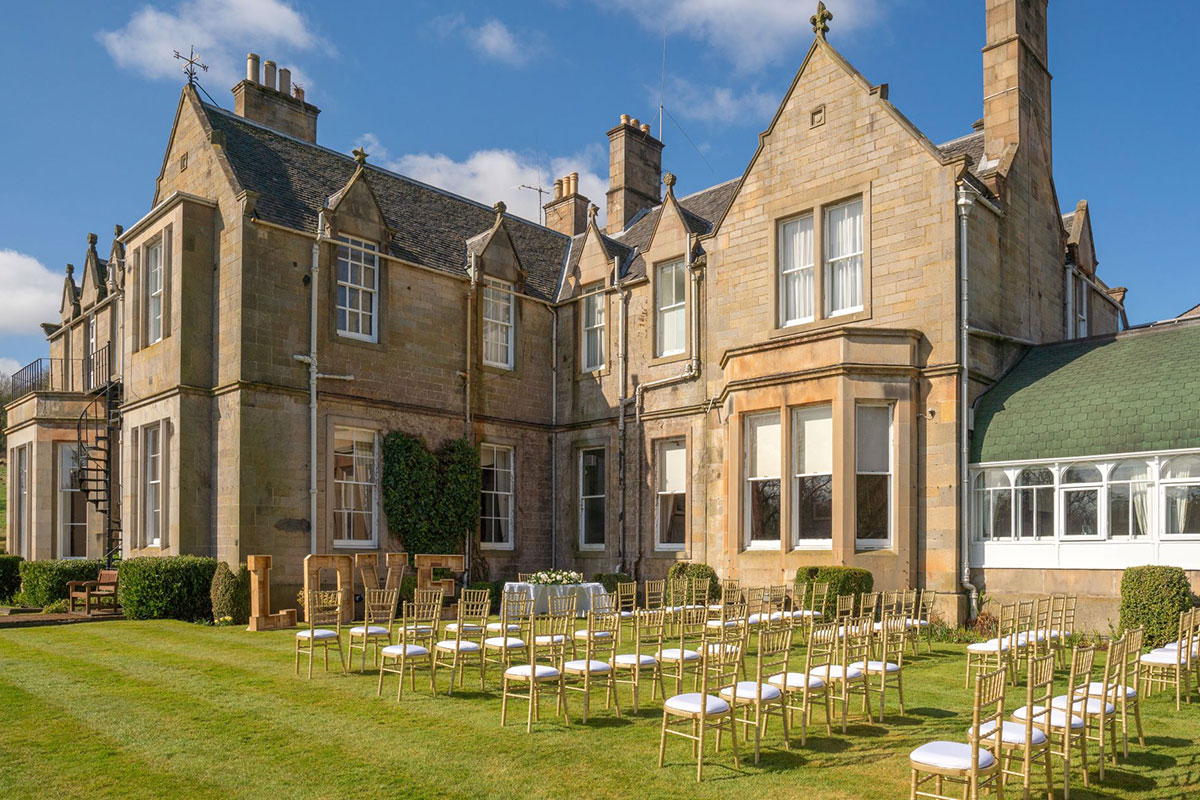 chairs set up outside on the lawn of a large brown sandstone house for an outdoor ceremony