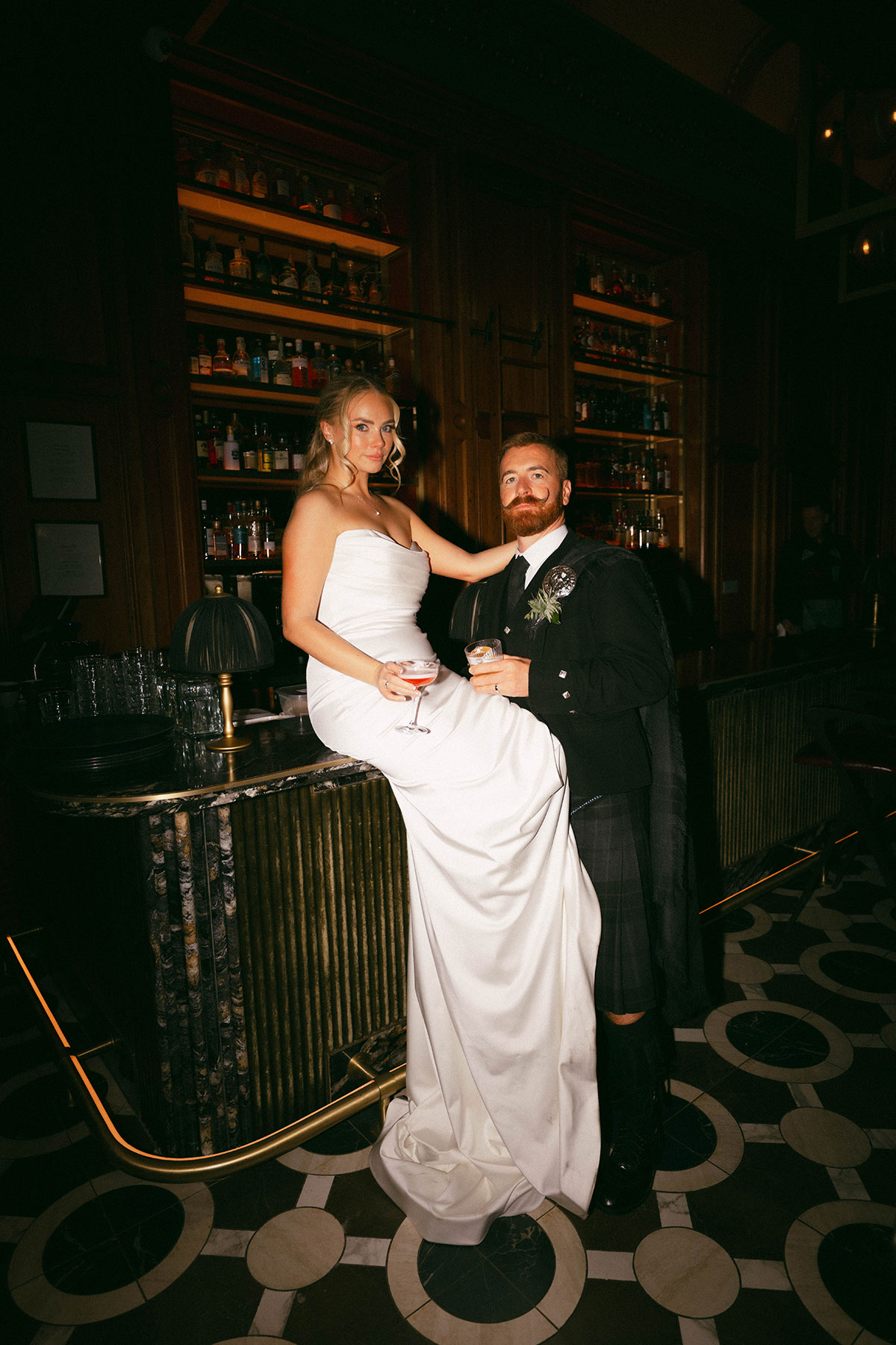bride and groom posing at bar with drinks in modern wedding reception space