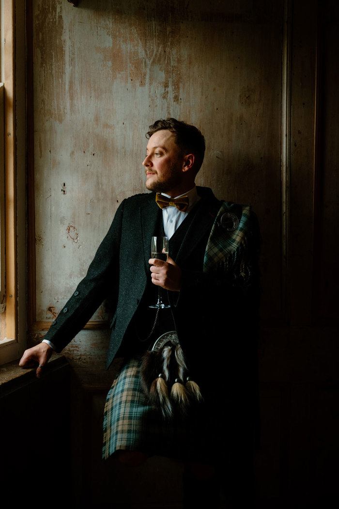 a groom in a kilt looking out of a window in a dark room at Neidpath Castle