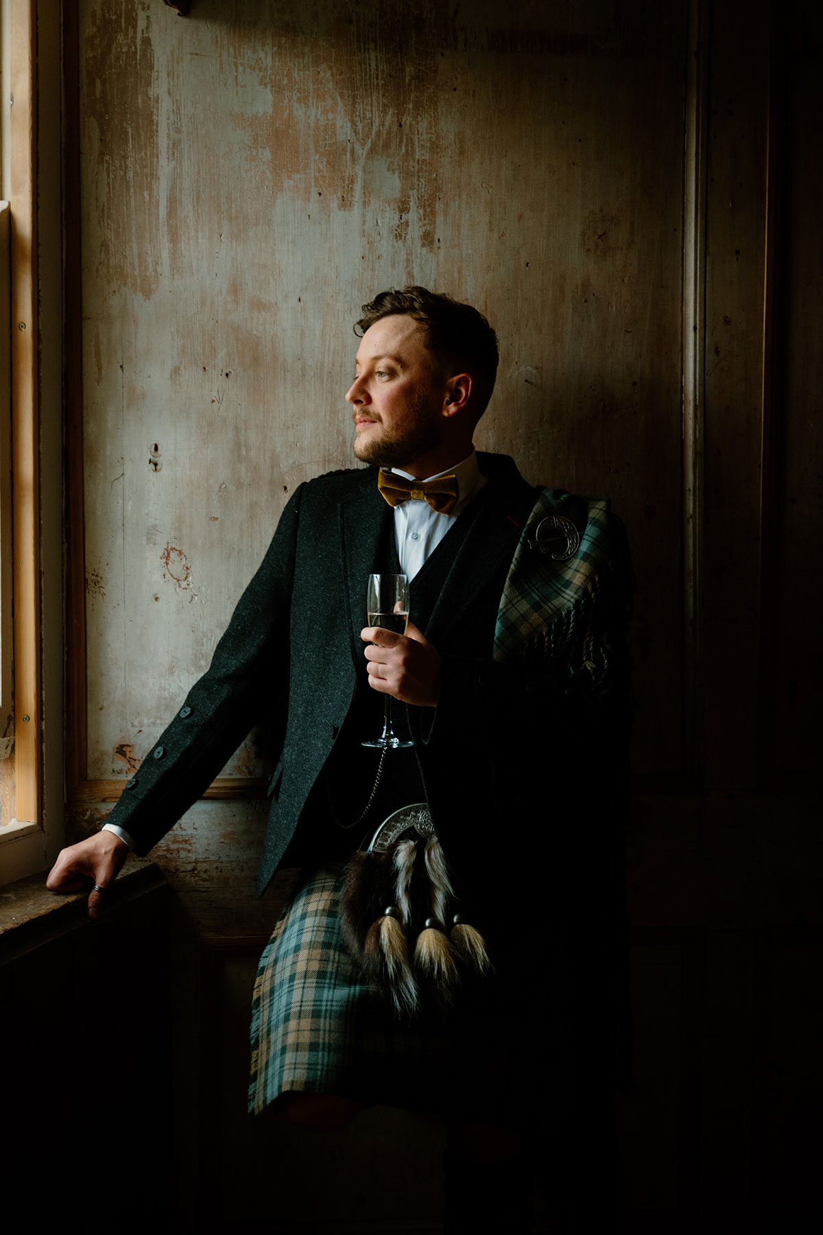 a groom in a kilt looking out of a window in a dark room at Neidpath Castle