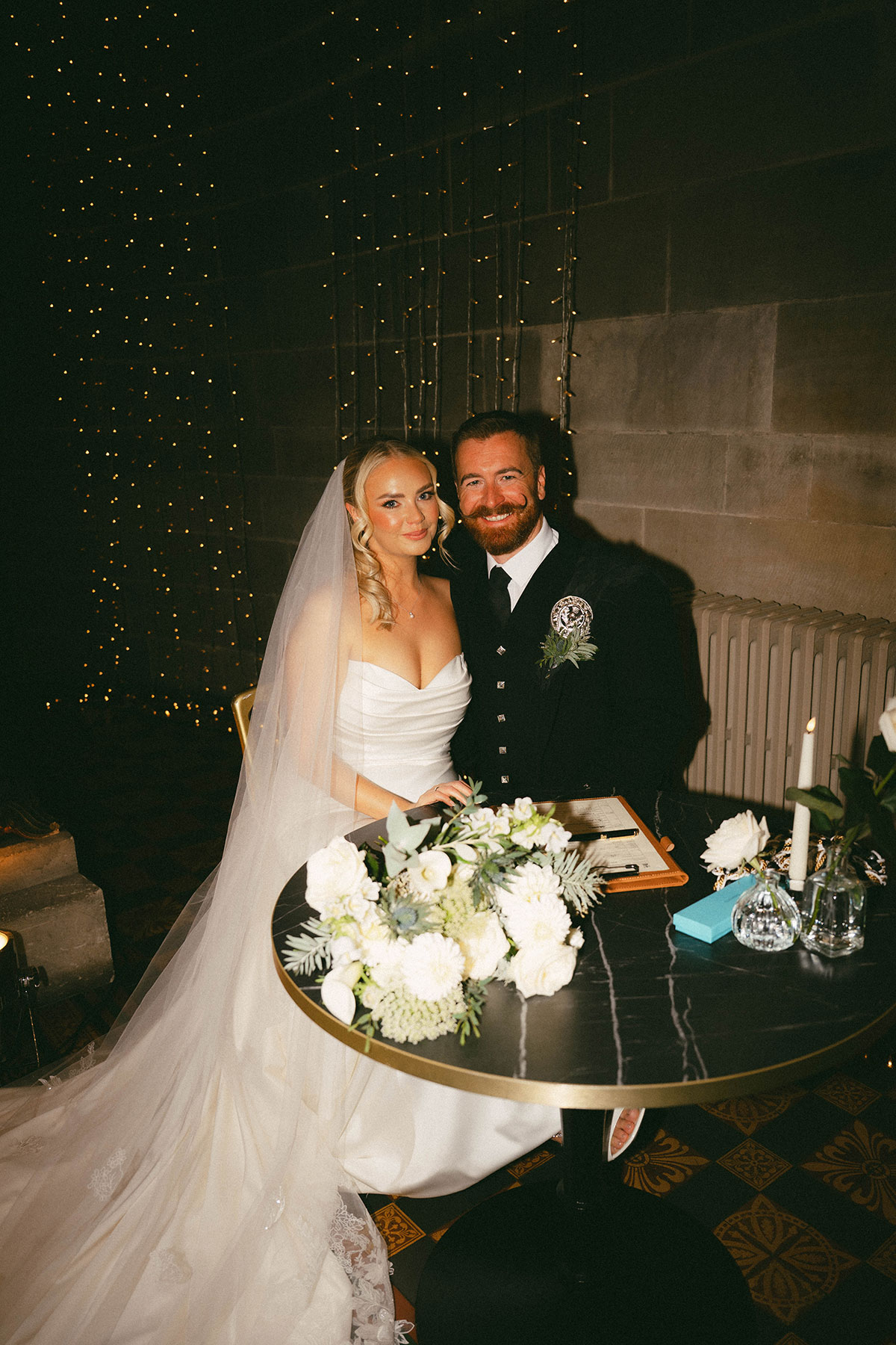 bride and groom signing wedding register at candlelit table with fairy lights