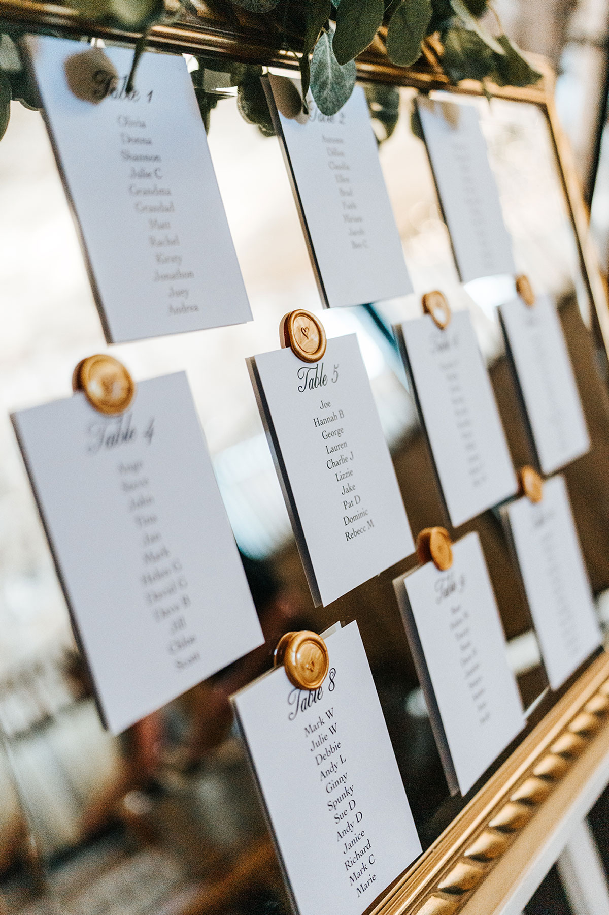 Close-up of wedding table plan cards with wax seal pins on a mirrored seating chart