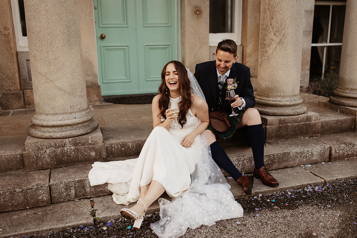 a bride and groom sitting on stone steps outside Netherdale House