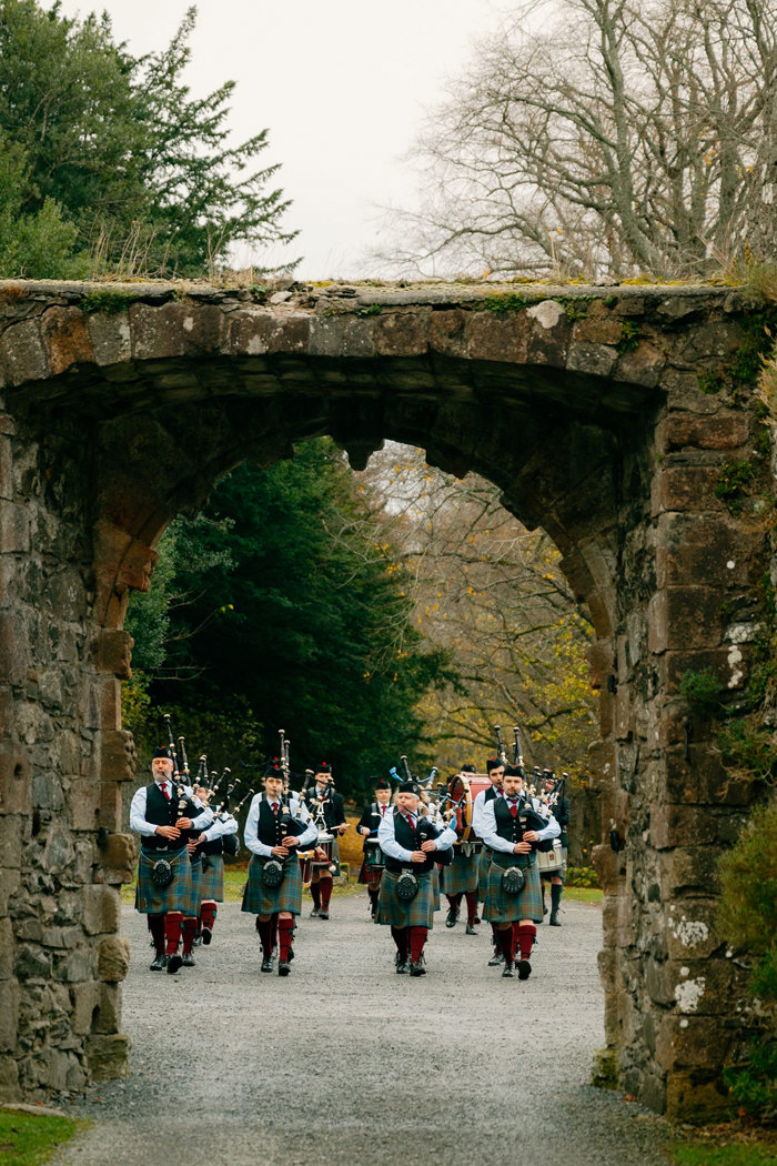 a pipe band walking towards a stone arch