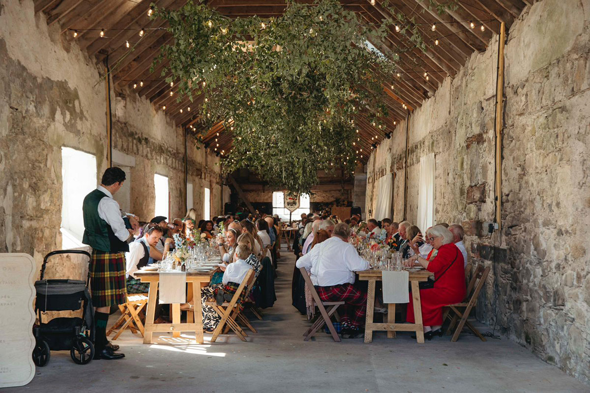 Long rustic tables set for wedding dinner inside stone barn decorated with greenery in the Cairngorms Highlands