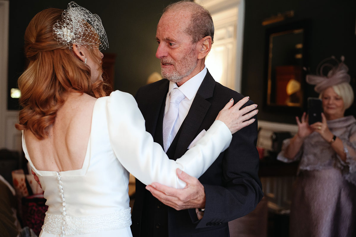A man in a suit and a woman in a white dress look at each other with their arms around each other