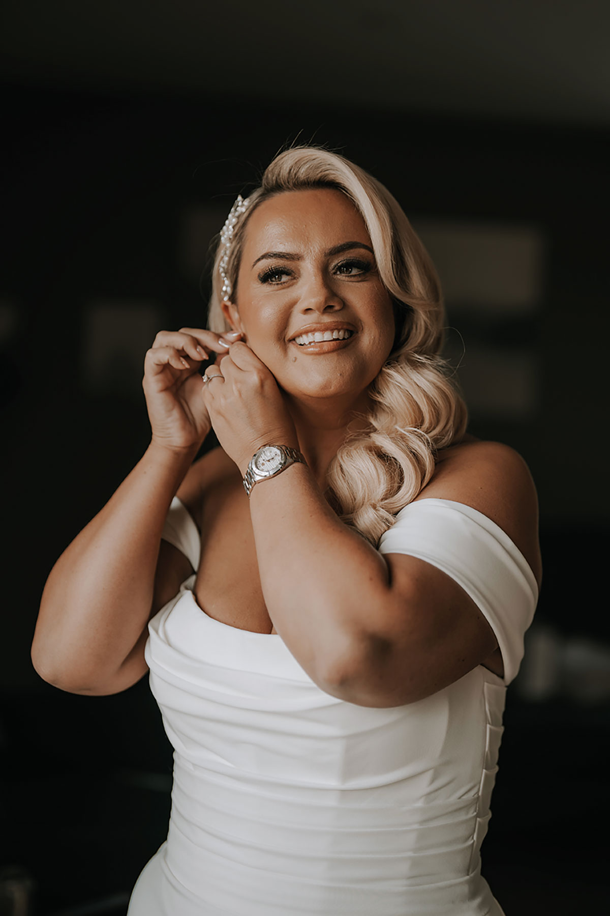 Bride smiling as she puts on earrings during her morning preparations.