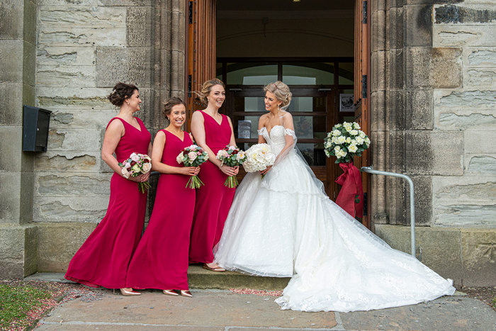 A Smiling Bride With Three Bridesmaids Wearing Red Resses Outside St Peters & St Andrews Church In Thurso