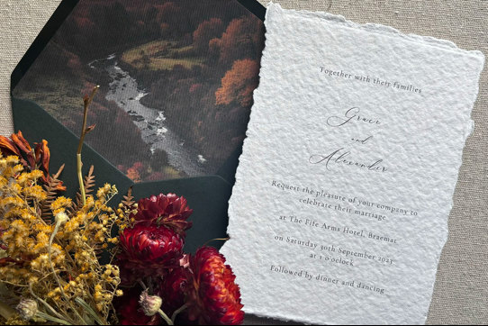 A wedding invitation out of a dark green envelope with red and yellow flowers to the left side