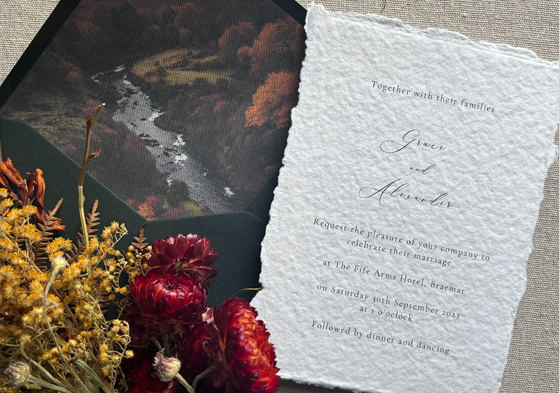 A wedding invitation out of a dark green envelope with red and yellow flowers to the left side