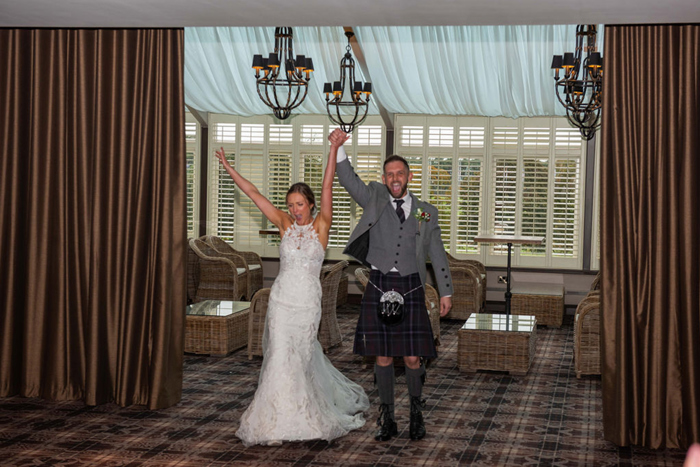 A Bride And Groom Cheering As They Walk Through Brown Silk Curtains