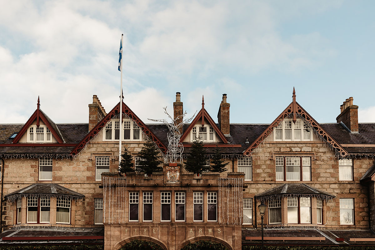 Front view of The Fife Arms with stone façade, peaked red gables and festive decorations under a bright winter sky