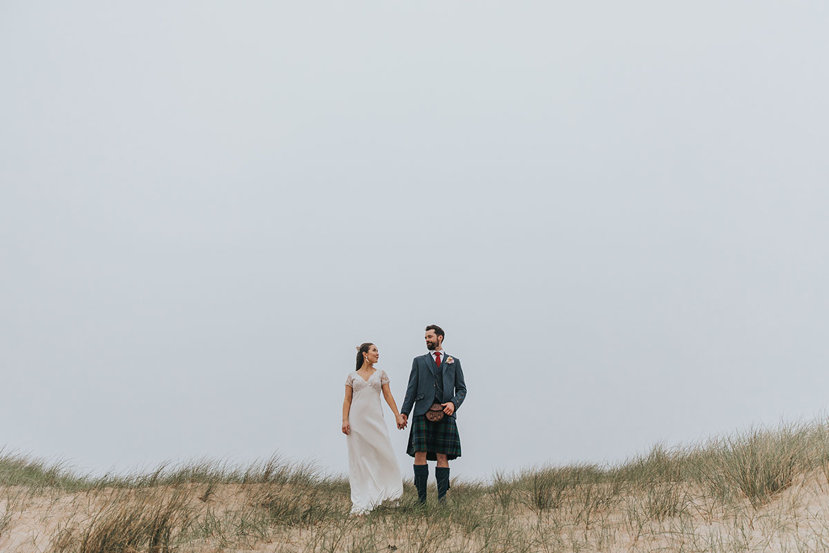 bride and groom hold hands while standing on the beach at harvest moon weddings