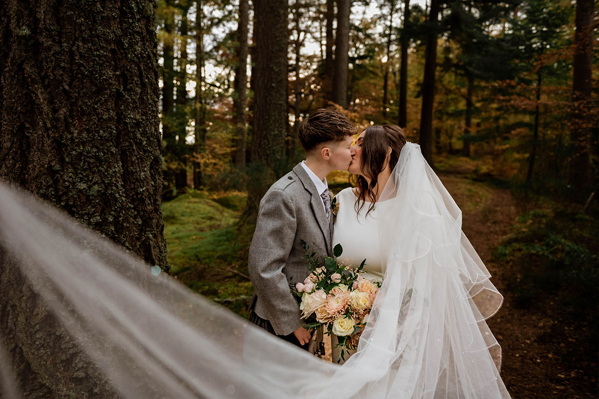 A couple kiss in a forest with sunlight coming through the trees
