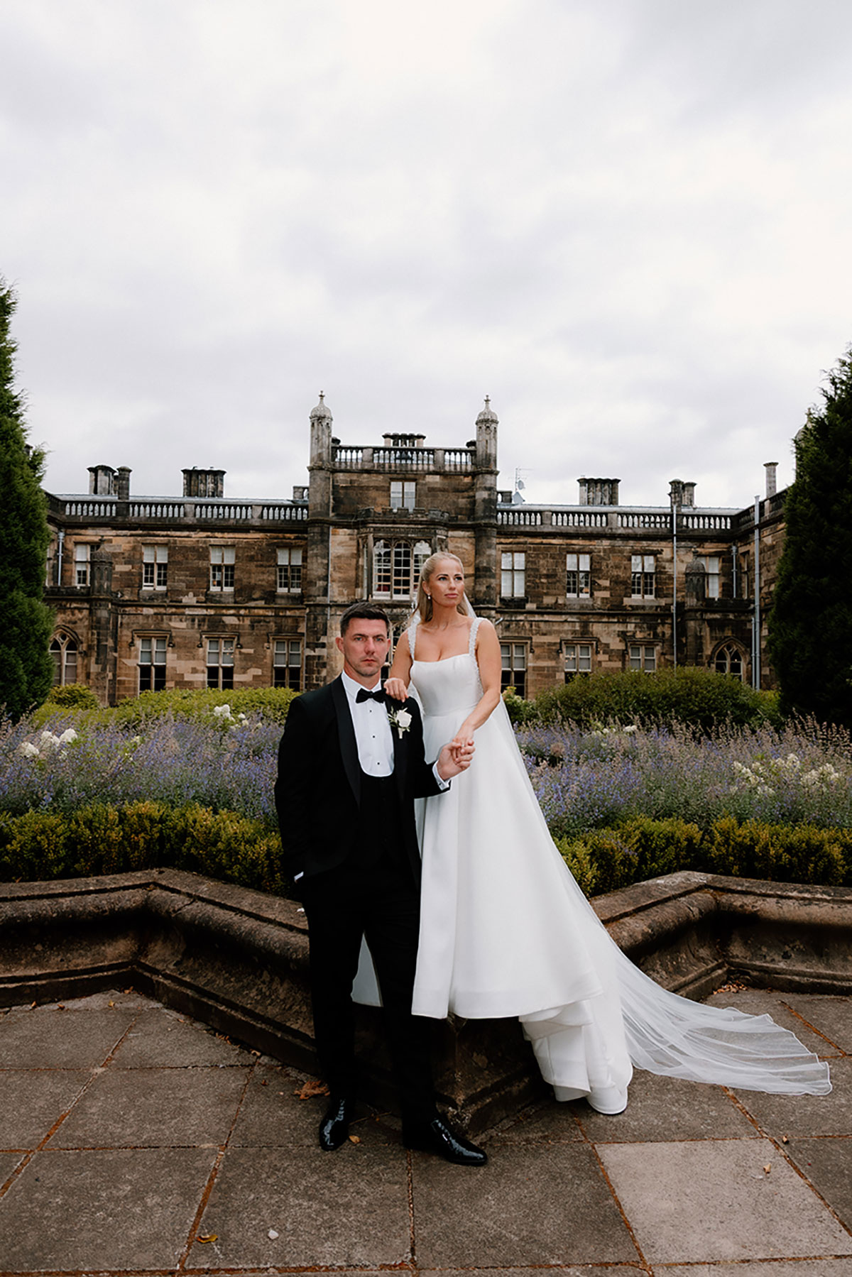 Bride and groom posing in front of the historic Mar Hall building with landscaped gardens behind them.
