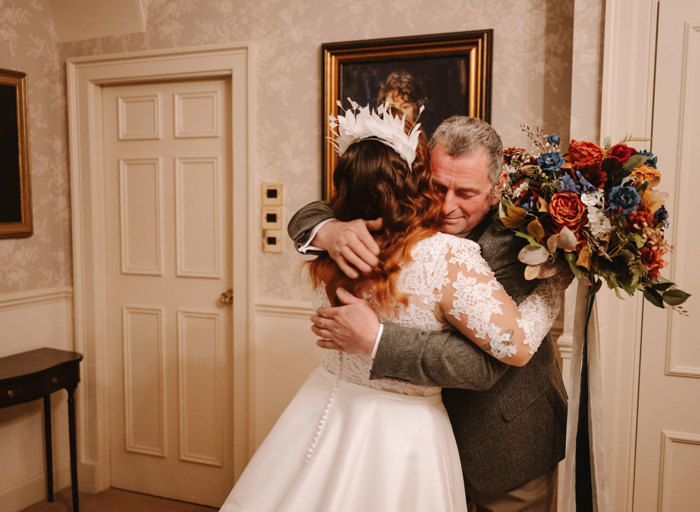 a man in a tweed jacket and woman in a lace wedding dress hugging
