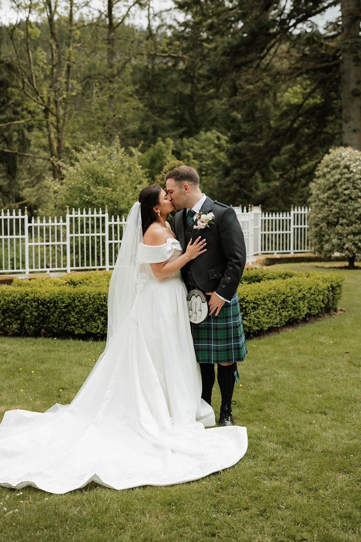 Bride and groom kissing in gardens at Drumtochty Castle Aberdeenshire with white fence backdrop