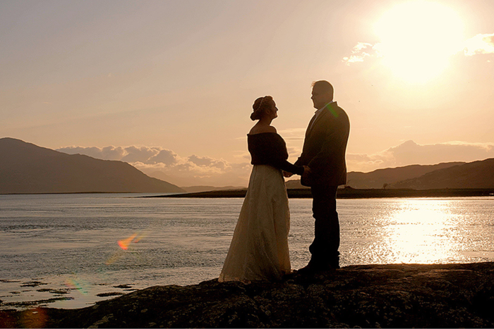 a couple holding hands standing next to water as the sunsets