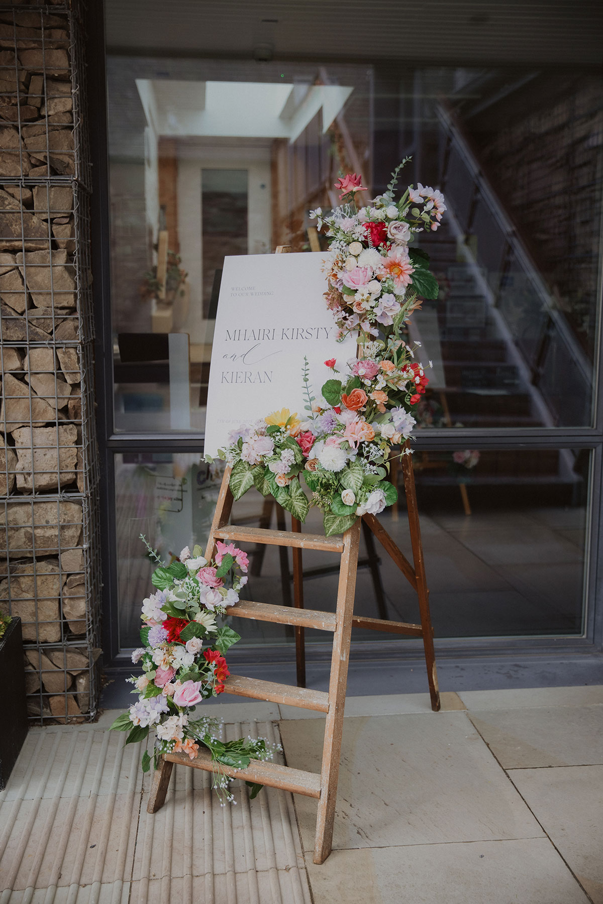 Floral wedding welcome sign on wooden easel decorated with bright summer flowers at Scottish venue entrance
