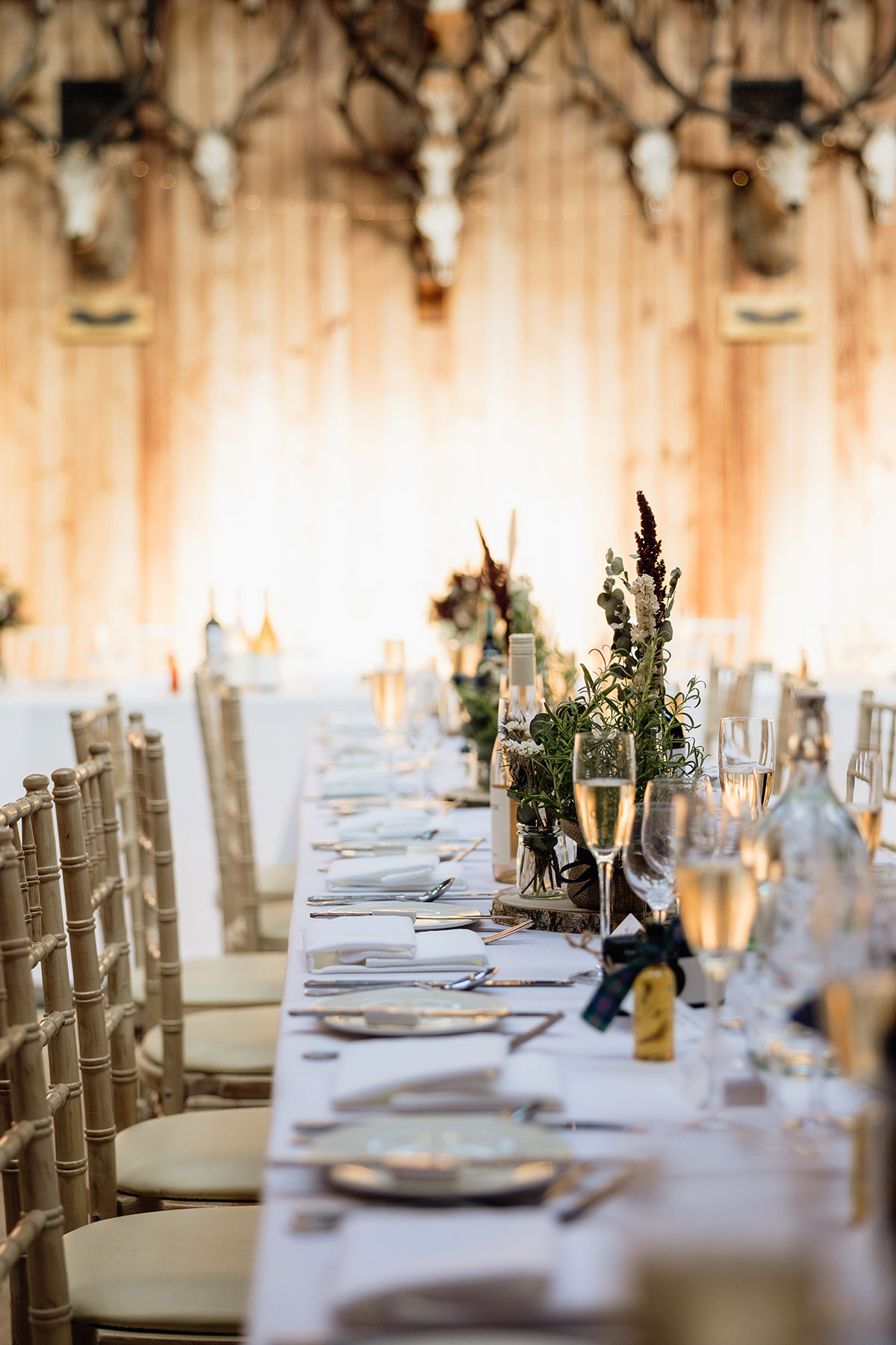 Long wedding reception table with elegant place settings and floral centrepieces inside the Great Hall at Mar Lodge Estate