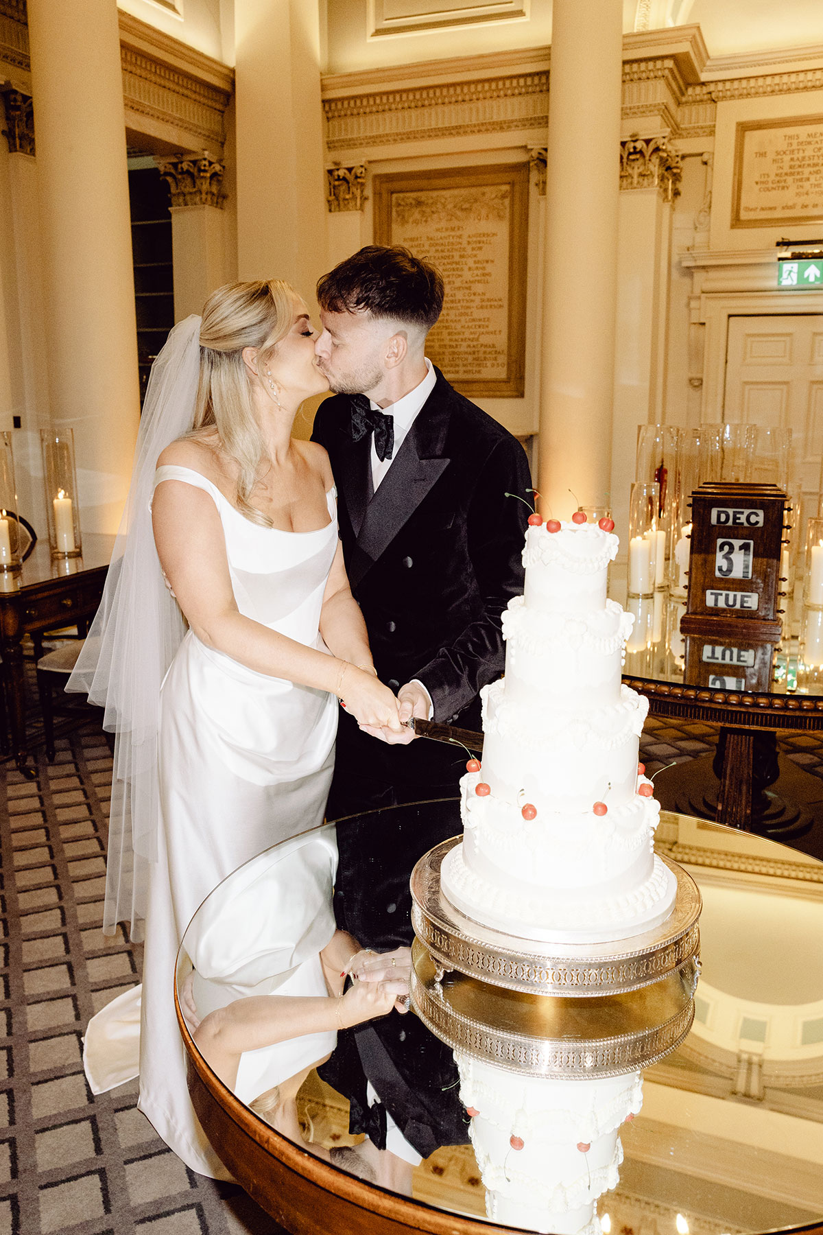 Bride and groom kissing as they cut their tiered white wedding cake decorated with cherries at the Signet Library