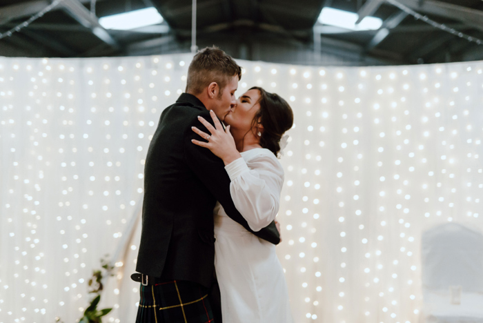 Couple kiss in front of fairy light wall