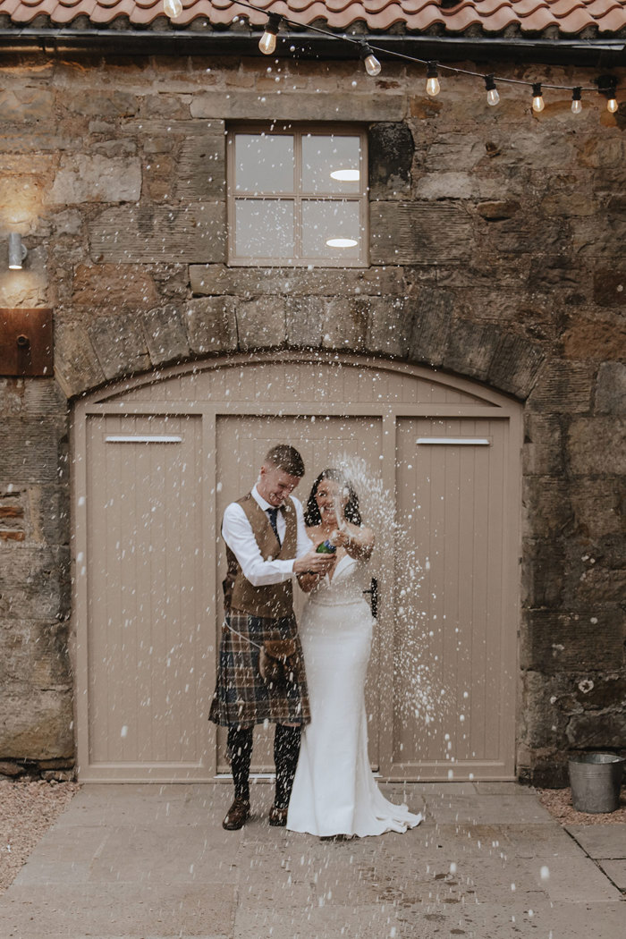 bride and groom spray champagne outside falside mill