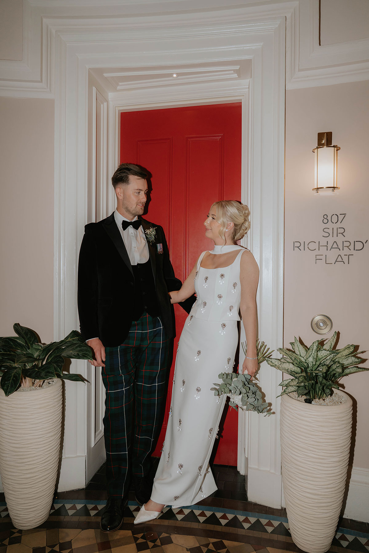 Bride and groom posing beside a red door in the stylish interior of their Edinburgh wedding hotel