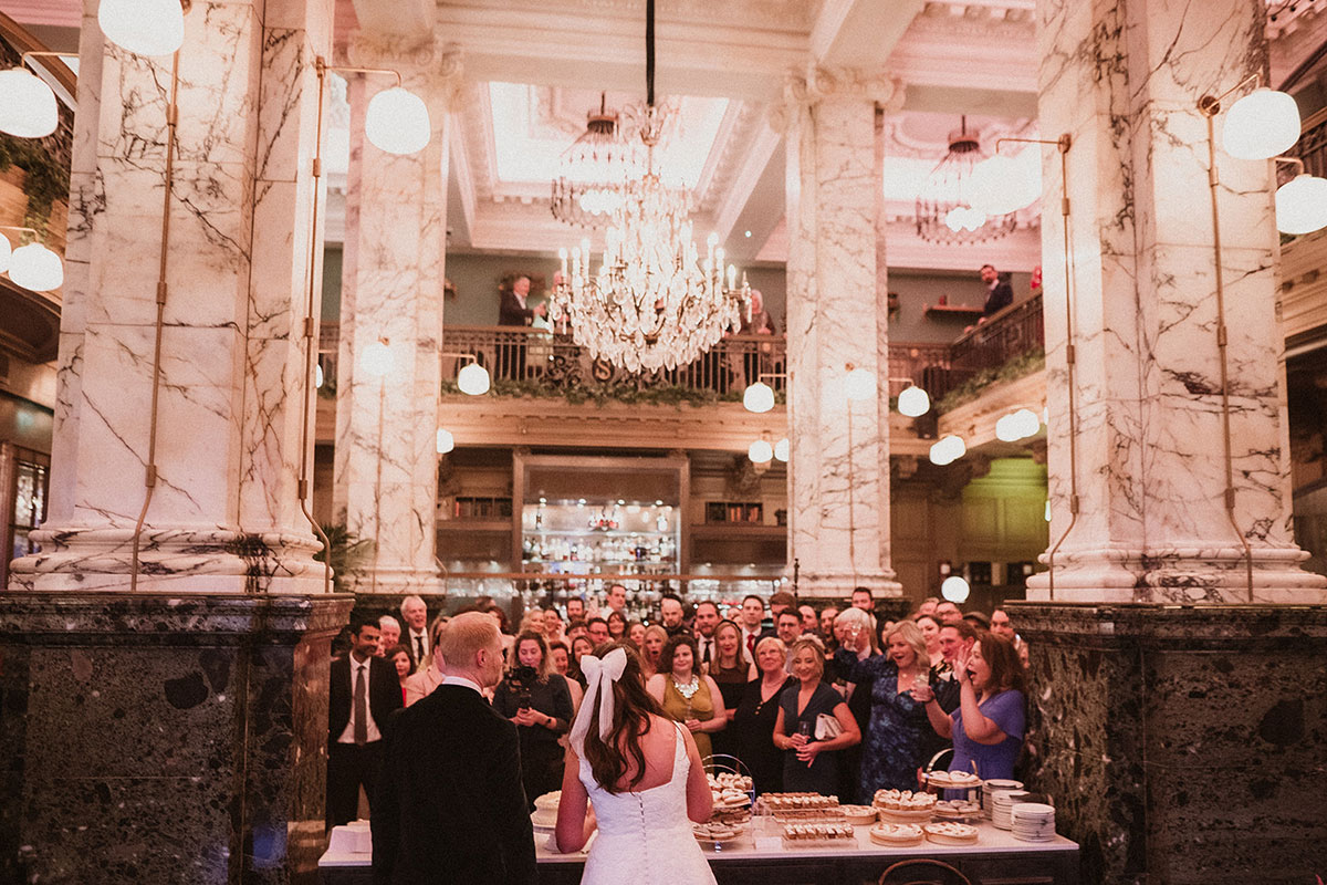 A bride and groom standing in a room with a large crowd of people at Scotsman Hotel in Edinburgh