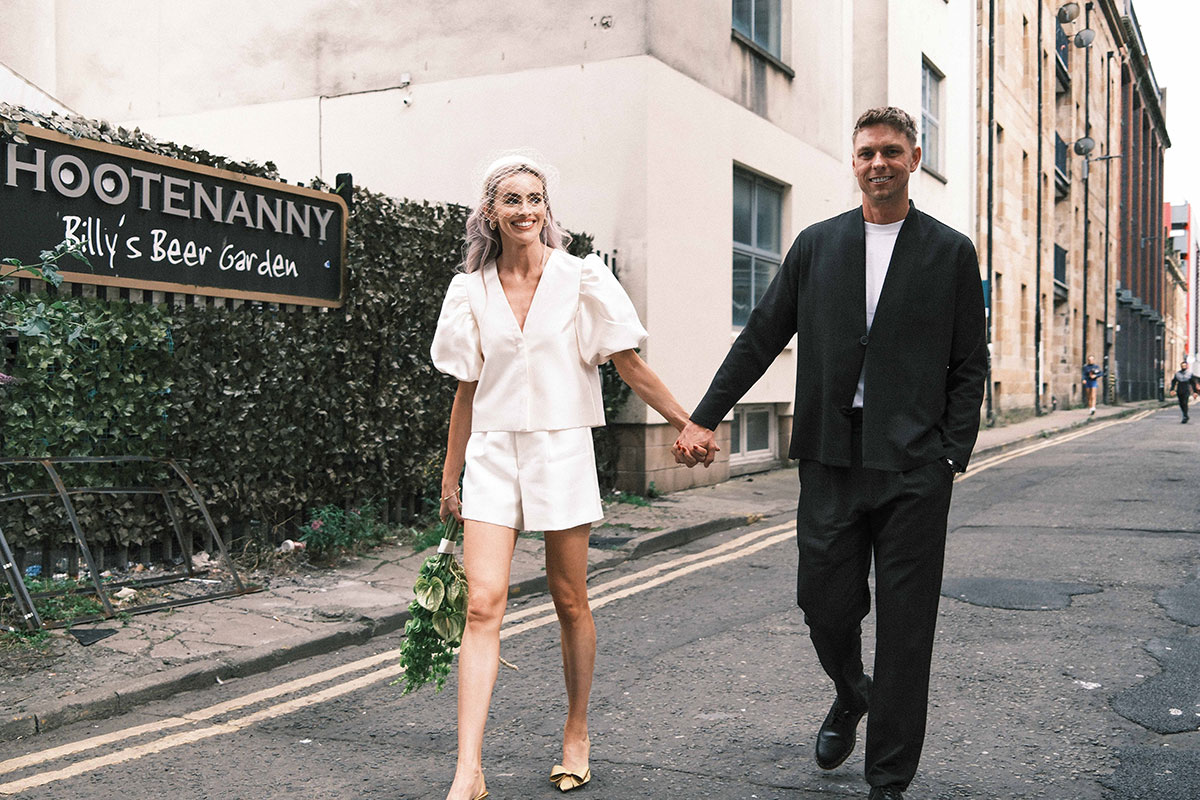 Bride in white shorts suit and groom walking through Glasgow city centre after intimate wedding ceremony